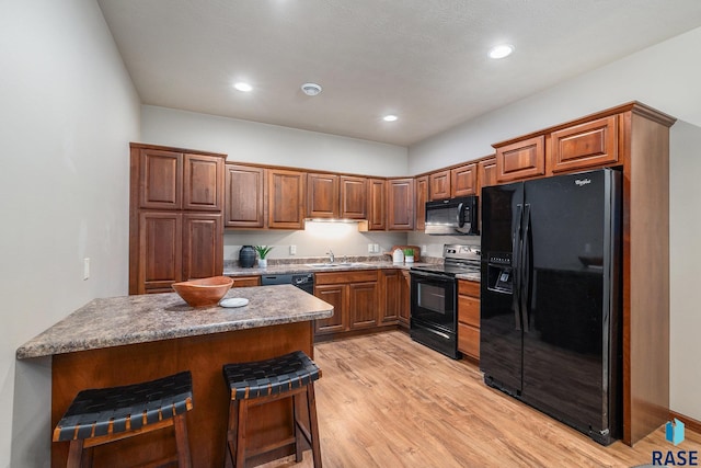 kitchen with sink, a breakfast bar area, light hardwood / wood-style floors, and black appliances