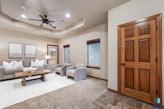 carpeted living room featuring ceiling fan and a tray ceiling