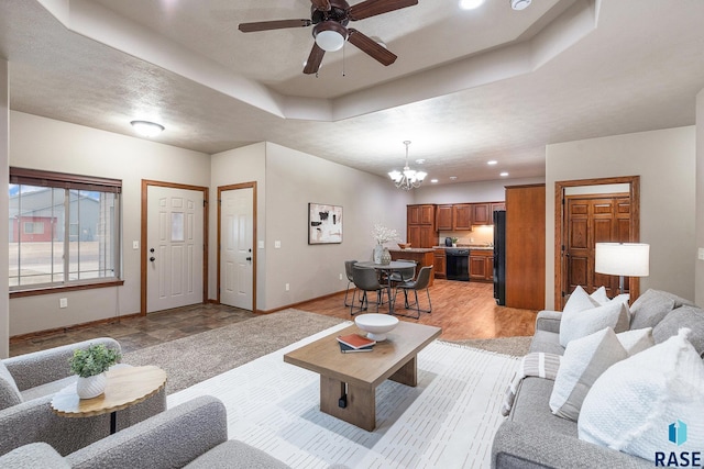 living room with a tray ceiling, ceiling fan with notable chandelier, and light hardwood / wood-style floors