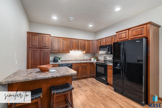 kitchen with sink, black appliances, a kitchen breakfast bar, and light wood-type flooring