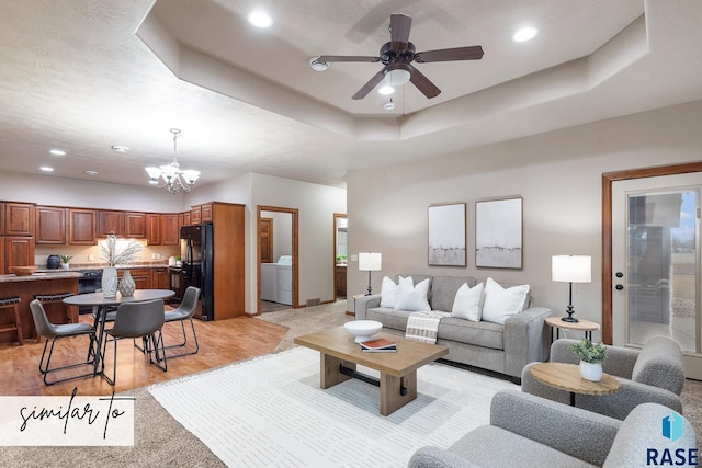 living room featuring light carpet, ceiling fan with notable chandelier, washing machine and dryer, and a raised ceiling