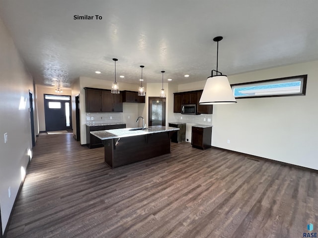 kitchen with tasteful backsplash, sink, a center island with sink, and decorative light fixtures