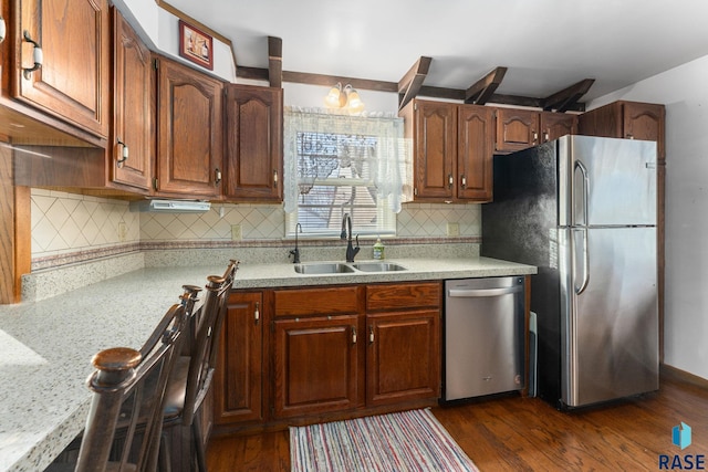 kitchen featuring dark wood-type flooring, sink, light stone counters, stainless steel appliances, and decorative backsplash