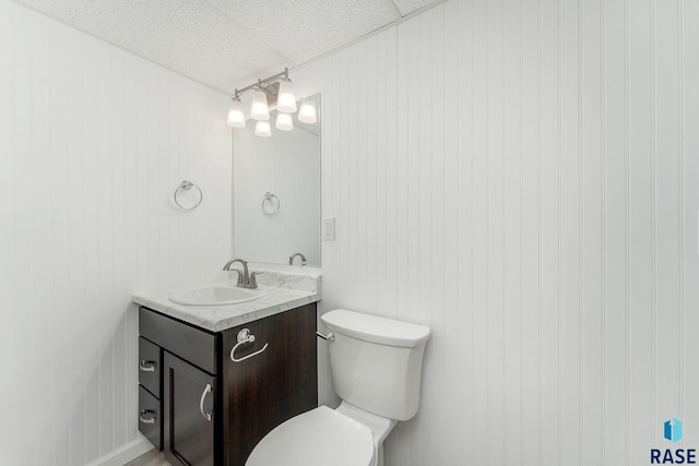 bathroom featuring wooden walls, a paneled ceiling, vanity, and toilet