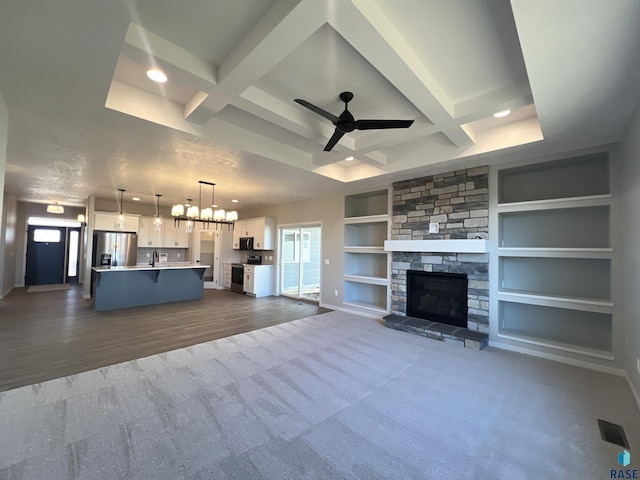 unfurnished living room with ceiling fan with notable chandelier, a stone fireplace, coffered ceiling, and built in features