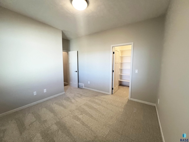 unfurnished bedroom featuring baseboards, a walk in closet, visible vents, and light colored carpet