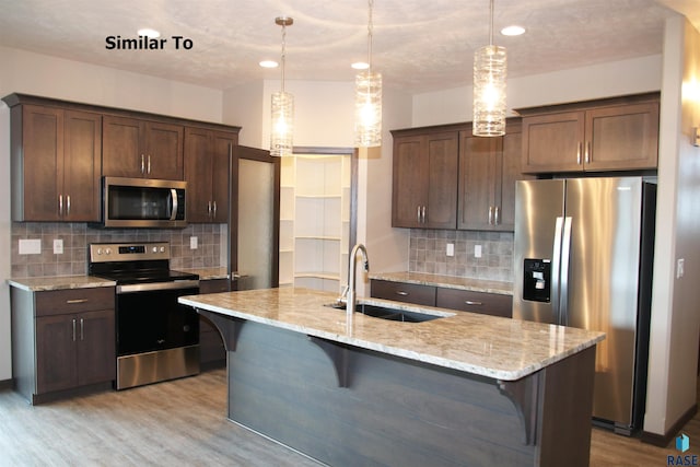 kitchen featuring stainless steel appliances, sink, light stone counters, and decorative light fixtures