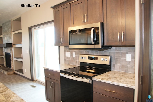 kitchen featuring light stone counters, light wood-style flooring, a large fireplace, stainless steel appliances, and backsplash