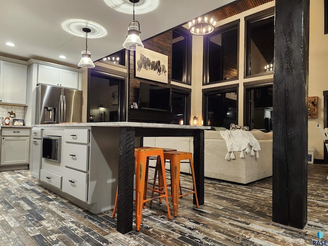 kitchen featuring a breakfast bar, white cabinetry, stainless steel refrigerator with ice dispenser, tasteful backsplash, and decorative light fixtures