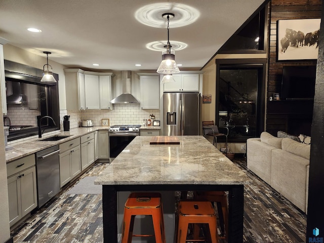 kitchen featuring wall chimney range hood, hanging light fixtures, backsplash, stainless steel appliances, and a kitchen breakfast bar