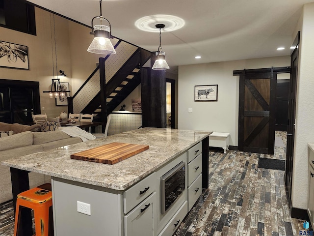 kitchen with light stone countertops, a barn door, a center island, and decorative light fixtures