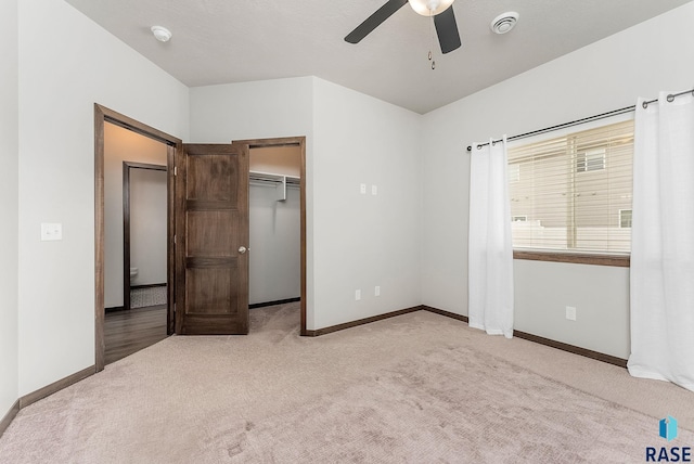 unfurnished bedroom with a walk in closet, light carpet, ceiling fan, and a closet