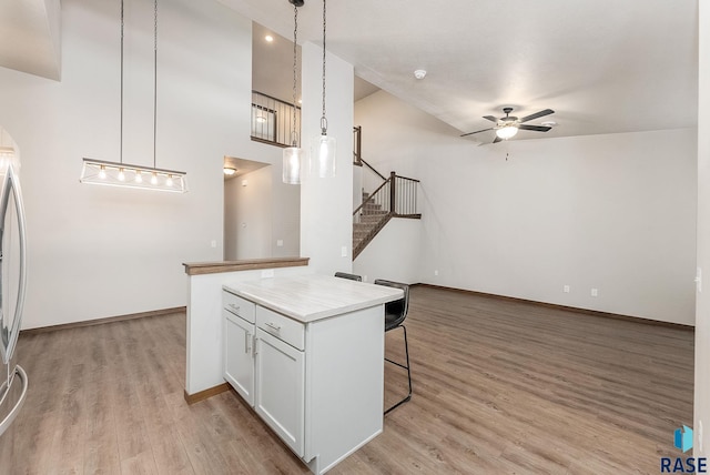 kitchen with a breakfast bar area, light hardwood / wood-style flooring, pendant lighting, ceiling fan, and white cabinets