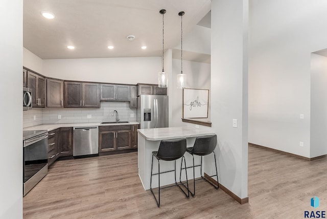 kitchen with sink, stainless steel appliances, tasteful backsplash, a kitchen bar, and decorative light fixtures