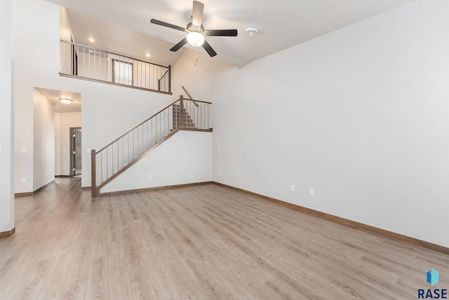 unfurnished living room with ceiling fan, a towering ceiling, and light wood-type flooring