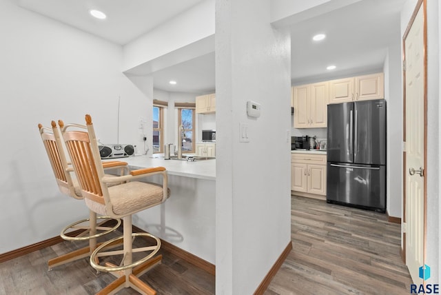 kitchen featuring hardwood / wood-style floors, stainless steel refrigerator, a kitchen bar, kitchen peninsula, and cream cabinets