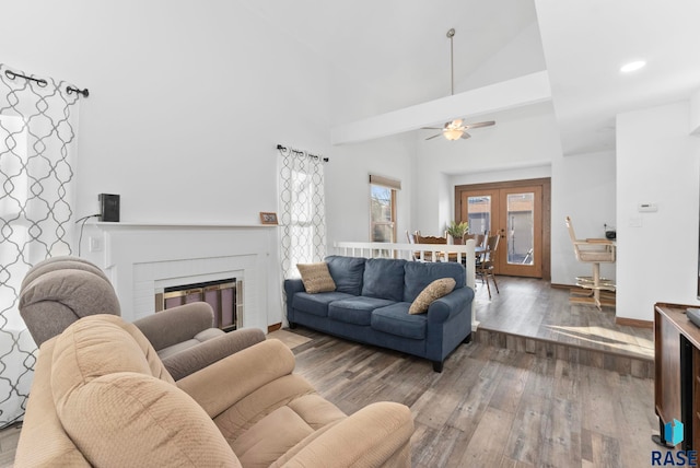 living room with hardwood / wood-style flooring, ceiling fan, high vaulted ceiling, and a brick fireplace