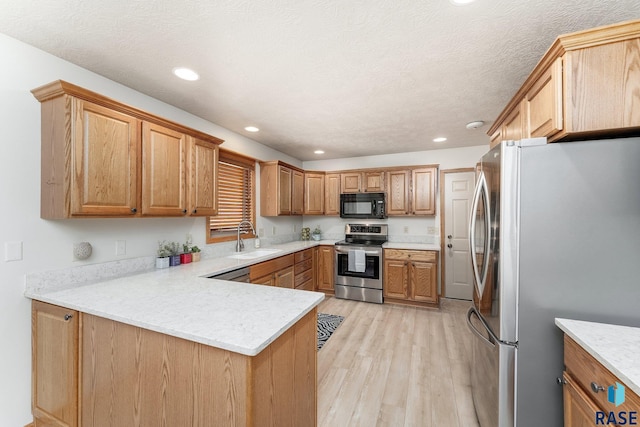 kitchen featuring sink, light hardwood / wood-style flooring, a textured ceiling, appliances with stainless steel finishes, and kitchen peninsula