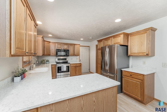 kitchen with sink, a textured ceiling, appliances with stainless steel finishes, kitchen peninsula, and light hardwood / wood-style floors