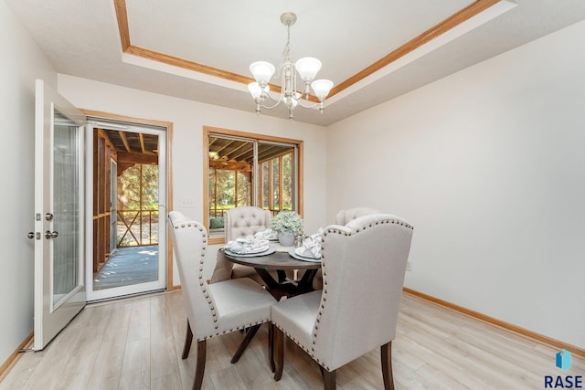 dining room with ornamental molding, a tray ceiling, a chandelier, and light hardwood / wood-style floors