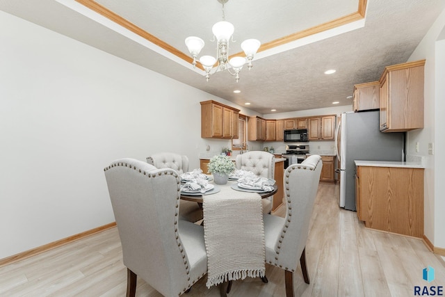 dining room with an inviting chandelier, crown molding, a textured ceiling, light hardwood / wood-style flooring, and a tray ceiling