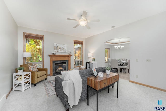 living room with a premium fireplace, carpet flooring, and ceiling fan with notable chandelier