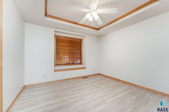 empty room with crown molding, ceiling fan, a tray ceiling, and light hardwood / wood-style flooring