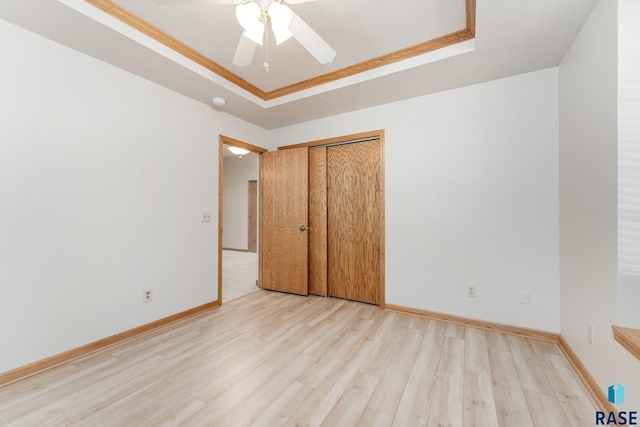 unfurnished bedroom featuring a closet, light hardwood / wood-style floors, ceiling fan, and a tray ceiling