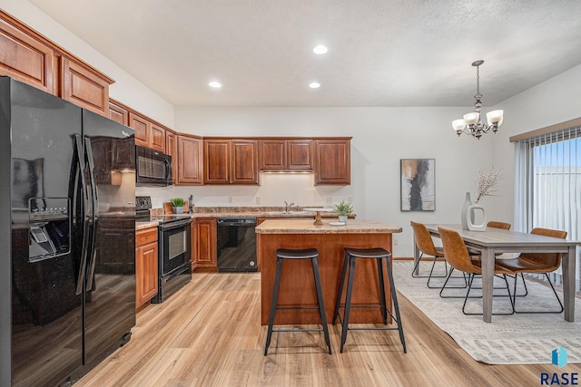 kitchen featuring pendant lighting, sink, black appliances, a kitchen island, and light wood-type flooring