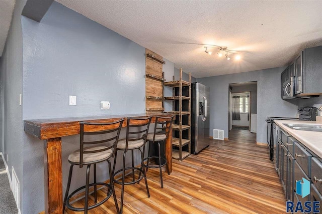 kitchen with light hardwood / wood-style flooring, a breakfast bar, stainless steel appliances, track lighting, and a textured ceiling