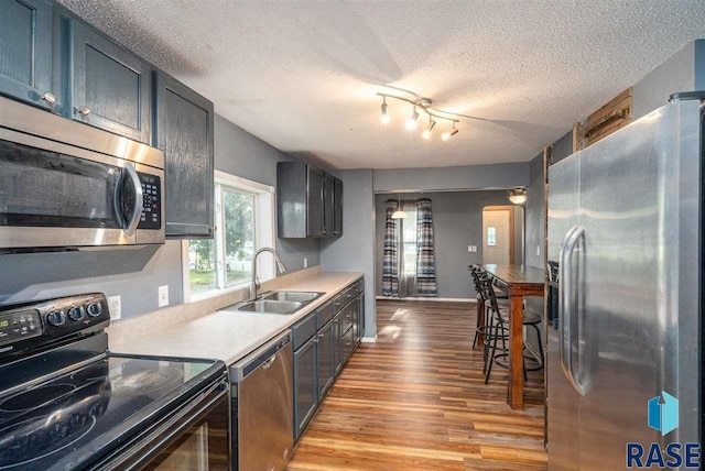 kitchen featuring stainless steel appliances, sink, a textured ceiling, and light wood-type flooring