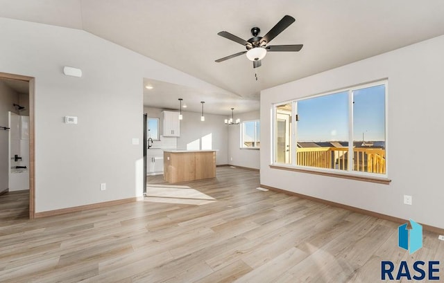 unfurnished living room featuring ceiling fan with notable chandelier, a healthy amount of sunlight, lofted ceiling, and light hardwood / wood-style floors