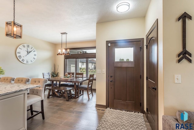 entrance foyer with an inviting chandelier, dark wood-type flooring, and a textured ceiling