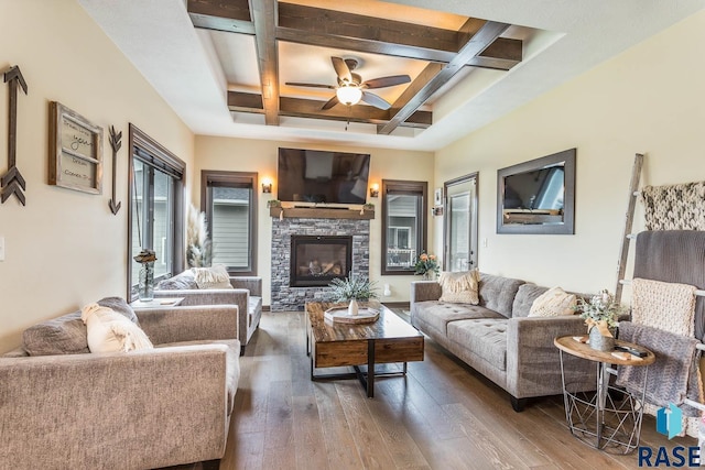 living room with a stone fireplace, dark hardwood / wood-style flooring, coffered ceiling, ceiling fan, and beam ceiling