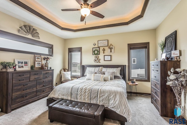 carpeted bedroom with ceiling fan and a tray ceiling