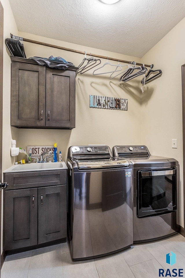 laundry room featuring light tile patterned floors, washer and clothes dryer, cabinets, and a textured ceiling