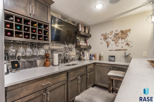 bar with dark brown cabinets, light stone countertops, sink, and a textured ceiling