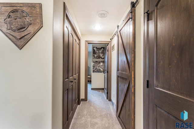 hallway featuring a barn door and light carpet