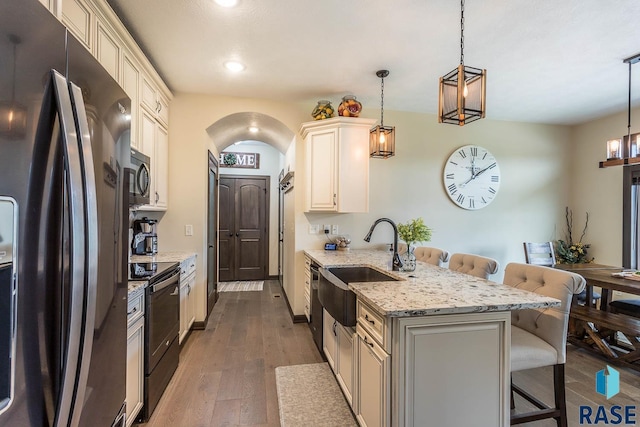 kitchen featuring a kitchen breakfast bar, hanging light fixtures, light stone counters, black appliances, and dark wood-type flooring