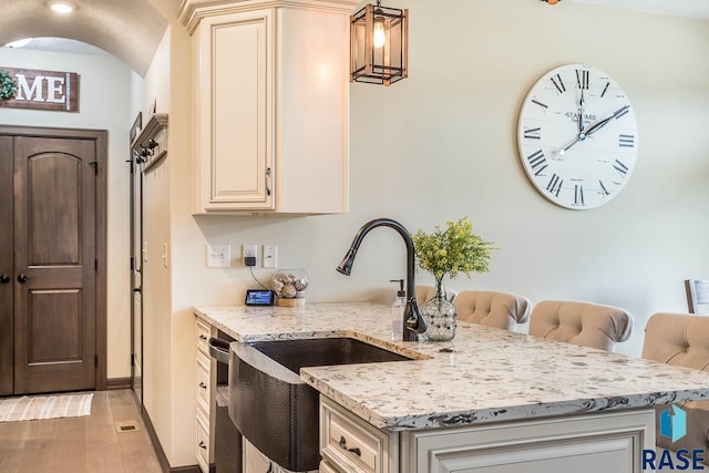 kitchen with light wood-type flooring, sink, light stone counters, and decorative light fixtures