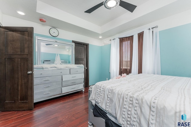 bedroom featuring dark hardwood / wood-style flooring, ceiling fan, and a tray ceiling