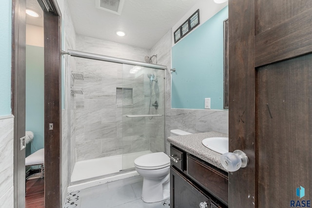 bathroom featuring vanity, toilet, tile walls, and a shower with shower door