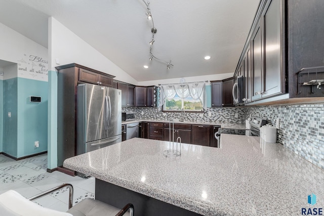 kitchen featuring appliances with stainless steel finishes, tasteful backsplash, lofted ceiling, kitchen peninsula, and light stone countertops