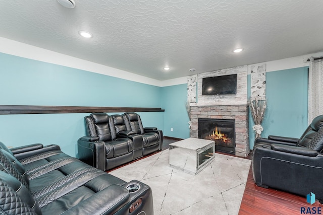 living room featuring wood-type flooring, a stone fireplace, and a textured ceiling