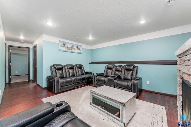 cinema featuring dark hardwood / wood-style flooring, a stone fireplace, and a textured ceiling