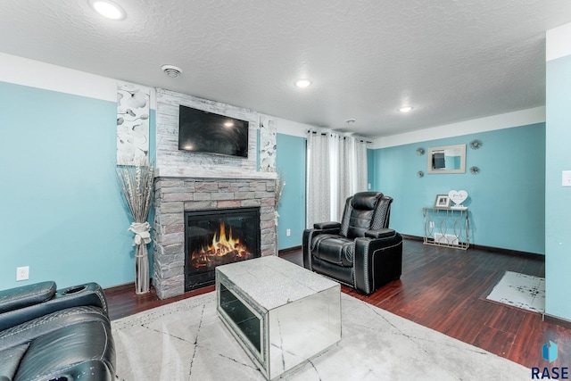 living room with hardwood / wood-style floors, a stone fireplace, and a textured ceiling