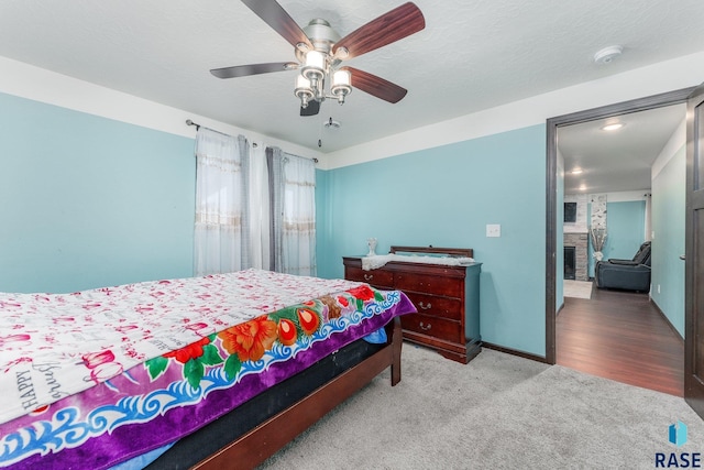 carpeted bedroom featuring ceiling fan and a fireplace