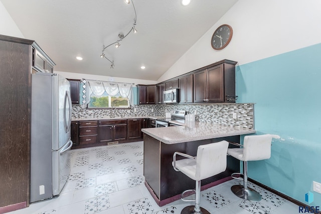 kitchen with sink, vaulted ceiling, appliances with stainless steel finishes, a kitchen breakfast bar, and kitchen peninsula