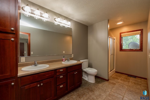 bathroom featuring vanity, toilet, a shower with door, and a textured ceiling