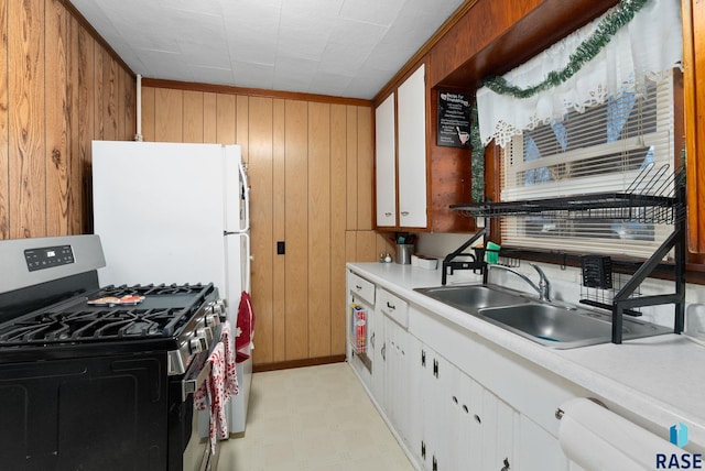 kitchen with white cabinetry, wooden walls, sink, and stainless steel gas stove